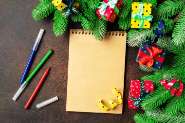 Açık defter, köknar dalları, koyu arkaplanda renkli ambalajlı hediye kutuları olan bir Noel ya da yeni yıl afişi. Hediye listesi veya Noel Baba 'ya mektup konsepti. Üst Manzara. Kopyalama alanı