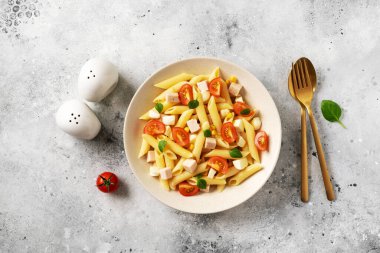 Jambonlu makarna salatası, mozzarella, mısır, domates ve hafif bir mutfak arka planında seramik tabakta zeytinyağı. Geleneksel İtalyan yemeği peynirli ve sebzeli makarna.