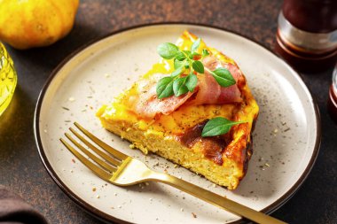 Koyu bir mutfak arka planında seramik tabakta balkabağı, domuz pastırması ve ricotta ile bir parça frittata. Geleneksel İtalyan lezzetli ev yapımı yumurta tabağı mutfak masasında.