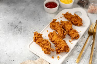 Hafif arka planda beyaz servis panosunda kızarmış tavuk filetosu ve ekmek kırıntıları. Mutfak masasında ev yapımı şeritler. Yakın plan.