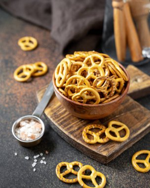 Koyu bir mutfak masasında, ahşap bir kasede tuzlu mini krakerler.