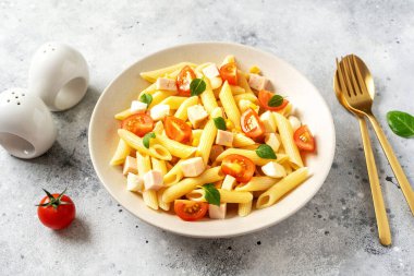 Jambonlu makarna salatası, mozzarella, mısır, domates ve hafif bir mutfak arka planında seramik tabakta zeytinyağı. Geleneksel İtalyan yemeği peynirli ve sebzeli makarna.