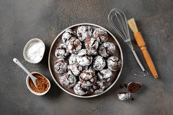 Homemade chocolate and coffee crinkle cookies in a white plate on the kitchen table. Traditional American cookies for Christmas with cracks and powdered sugar on a culinary background top view