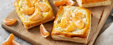 Mutfak masasındaki tabakta peynirli krema, badem ve mandalinalı mini puf böreği. Turunçgil meyveli, dormavi ya da ricotta soslu, fındıklı ve aşçı arkaplanlı lezzetli bir kare. Pankart