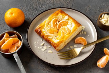 Mutfak masasındaki tabakta peynirli krema, badem ve mandalinalı mini puf böreği. Limon meyveli, dorblue ya da ricotta soslu, fındık aromalı, lezzetli bir kare.