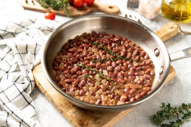 Stewed red beans with onion and thyme in tomato sauce in a frying pan on a bright kitchen table closeup