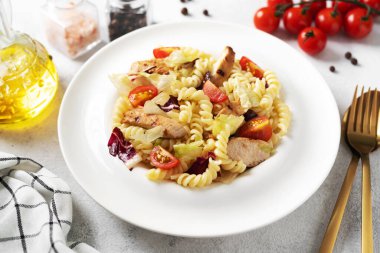 Pasta salad with grilled chicken, tomatoes and olive oil in a plate on a light culinary background. Traditional Italian dish girandole or fusili fried poultry fillet and vegetables closeup