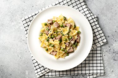 Yeşil bezelyeli Farfalle, hindi jambonu ve krema soslu parmesan. Mutfak masasındaki beyaz tabakta. Hafif bir mutfak arka planında geleneksel İtalyan makarnası. Üst görünüm