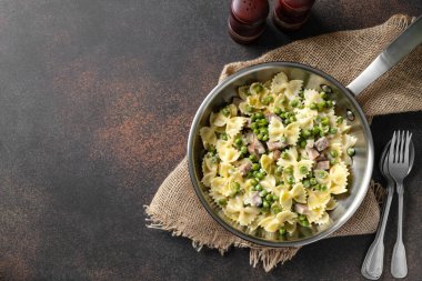 Yeşil bezelyeli Farfalle, hindi jambonu ve krema soslu parmesan mutfak masasındaki tavada. Copyspace 'in arka planında koyu renk bir İtalyan makarnası.