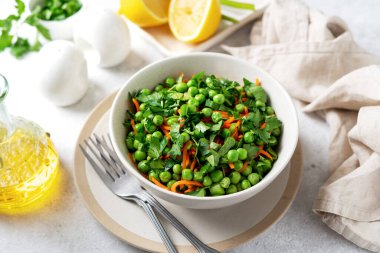 Yeşil bezelyeli bir kase salata, havuç turşusu ve parlak mutfak masasında zeytinyağlı maydanoz. Sağlık ve kilo kaybı için enfes sağlıklı salata.