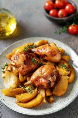 Fırında tavuk budu ve patates, portakal, sarımsak ve soğan ile birlikte karanlık bir mutfak arka planında.