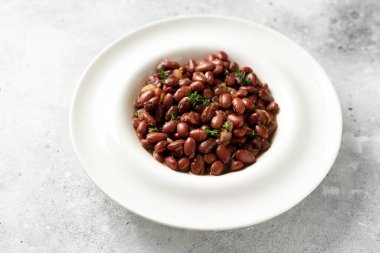 Mutfak masasındaki beyaz tabakta soğanlı ve kekik soslu kırmızı fasulye.