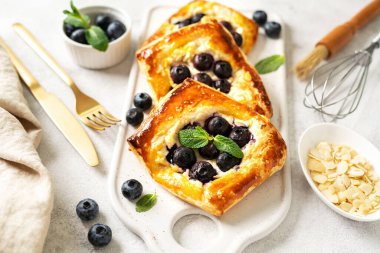 Mutfak masasında peynirli krema, badem ve yaban mersinli mini puf böreği. Lezzetli katmanlı kare, böğürtlen, dorblue veya ricotta, aşçılık arka planında fındık.
