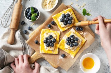 Peynirli krema ve yabanmersinli çiğ puf böreği. Lezzetli çörekler ya da mini turtalar yapma süreci. Pişirme hamurunun kenarlarını yumurta ile yağlamak. Eller çerçevede.