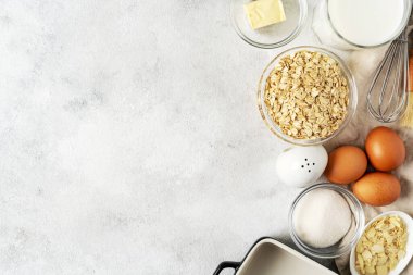 Açık gri mutfak zemininde puding ya da yulaflı turta için malzemeler. Yumurta, tahıl, badem, şeker, süt ve tereyağı mutfak masasında. Kopyalama uzayından en üstteki görünüm