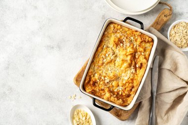 Açık gri mutfak arka planında bir kabın içinde puding ya da yulaf ezmesi turtası. Mutfak masasının üstünde fındıklı mısır gevreği ve fotokopi alanı. Sağlıklı ve besleyici bir kahvaltı.