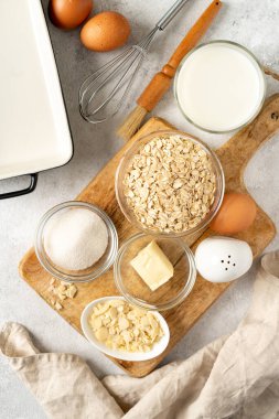  Açık gri mutfak zemininde puding ya da yulaflı turta için malzemeler. Yumurta, tahıl, badem, şeker, süt ve tereyağı mutfak masasında. Üst görünüm