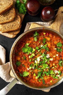 Fasulye, sebze ve kişniş soslu ev yapımı vejetaryen güveç. Arka planda siyah bir tavada.