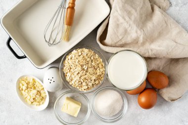 Açık gri mutfak zemininde puding ya da yulaflı turta için malzemeler. Yumurta, tahıl, badem, şeker, süt ve tereyağı mutfak masasında. Üst görünüm
