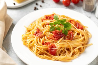 Domatesli spagetti, parmesan peyniri ve fesleğen parlak bir mutfak masasında beyaz bir tabakta. Geleneksel İtalyan makarnası, sebze ve peynir.