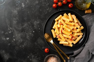 Domatesli tortiglioni, ricotta ve fesleğen siyah bir tabakta, karanlık bir mutfak masasında. Geleneksel İtalyan makarnası, sebzeli ve kremalı süzme peynirli. Kopyalama uzayından en üstteki görünüm