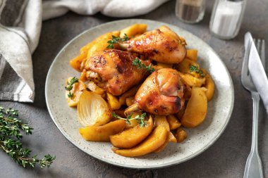Fırında tavuk budu ve patates, portakal, sarımsak ve soğan ile birlikte karanlık bir mutfak arka planında.