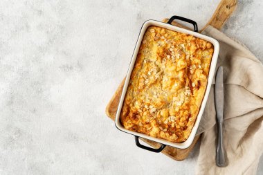 Açık gri mutfak arka planında bir kabın içinde puding ya da yulaf ezmesi turtası. Mutfak masasının üstünde fındıklı mısır gevreği ve fotokopi alanı. Sağlıklı ve besleyici bir kahvaltı.