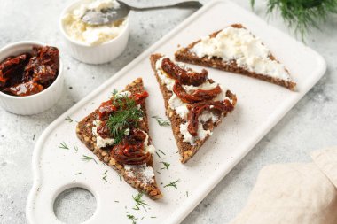Ya da krem peynirli ve güneşte kurutulmuş domatesli tam tahıllı sandviç. Crostini servis masasında, açık mutfak masasının üstünde.