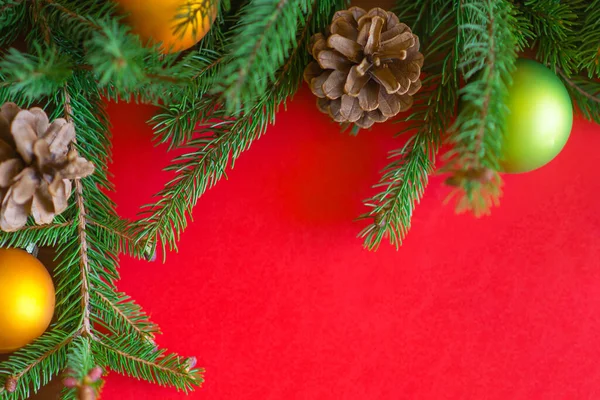 クリスマスの背景 赤い背景にコーンとクリスマスボールと緑の松の枝 境界線とコピースペース トップビューを持つ創造的な組成 — ストック写真