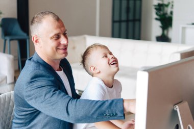 Mutlu baba bilgisayar başında oturur ve yanında mutlu bir anaokulu çocuğu, monitöre bakar ve gülümser..