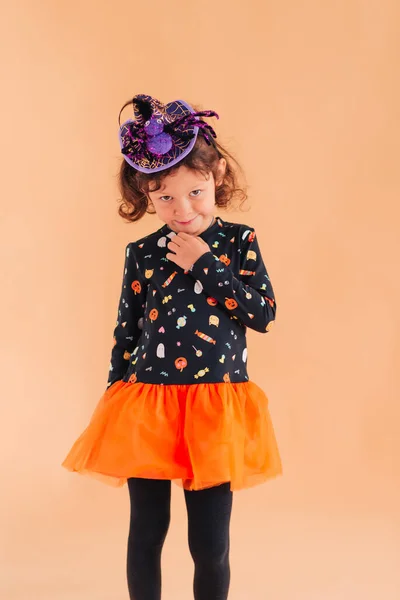 一个穿着巫婆服装 头戴蜘蛛帽 头戴南瓜杰克 背景朴素的有趣小女孩 — 图库照片