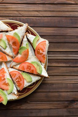Krem peynirli kanepe, domates ve beyaz tost üzerinde avokado, ahşap arka planda bir tabakta.