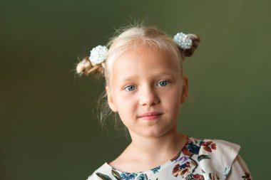 Parlak duyguları olan sevimli küçük sarışın. Sürpriz, neşe, mutluluk, ilgi. Çiçek desenli bir elbise giymişti. Yeşil arka plan. Avrupa yarışı.