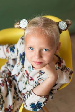 Parlak duyguları olan sevimli küçük sarışın. Sürpriz, neşe, mutluluk, ilgi. Çiçek desenli bir elbise giymişti. Yeşil arka plan. Avrupa yarışı.