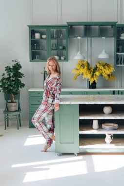 Evdeki mutfakta güzel, modern bir kadın. Ekose pijamalar. İç kısımda sarı çiçekler var. Tablo, yemekler, tasarım.