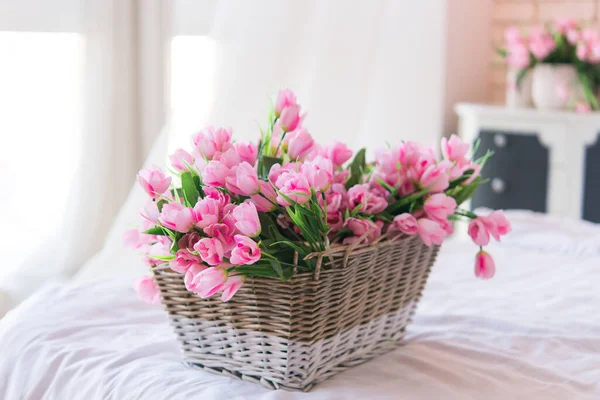 Basket with tulips. Soft home decor, wicker straw basket, on bed with white linens. Interior.
