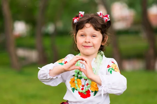 緑の背景にウクライナの民族衣装で楽しい若い女の子の肖像画 屋外だ 笑顔だ 両手で印を示す — ストック写真