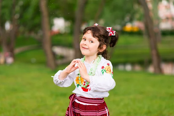 緑の背景にウクライナの民族衣装で楽しい若い女の子の肖像画 屋外だ 笑顔だ 両手で印を示す — ストック写真