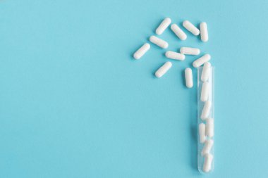 Beyaz kapsül mavi arka plandaki şeffaf plastik bir şişeden..