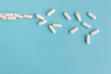 Farklı beyaz haplar ve mavi arka planda plastik bir kap. Tıbbi tema.