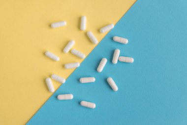 Sarı ve mavi renkli arka planda beyaz haplar. Kapsüller hapları yakın plan çeker. Sağlık ve İlaç.