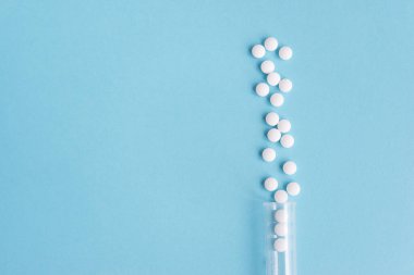 Farklı beyaz haplar ve mavi arka planda plastik bir kap. Tıbbi tema.