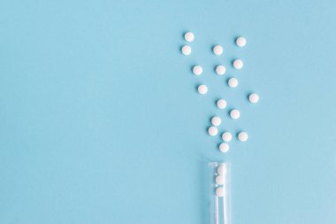 Farklı beyaz haplar ve mavi arka planda plastik bir kap. Tıbbi tema.