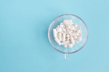 Farklı beyaz haplar ve mavi arka planda plastik bir kap. Tıbbi tema.