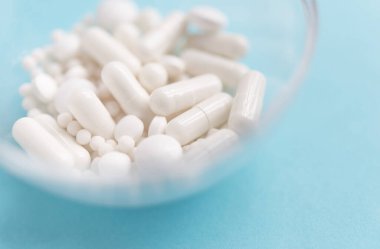 Farklı beyaz haplar ve mavi arka planda plastik bir kap. Tıbbi tema.