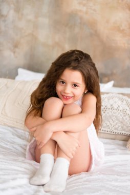 Anaokulu kızı bacak bacak üstüne atmış yatakta oturuyor.