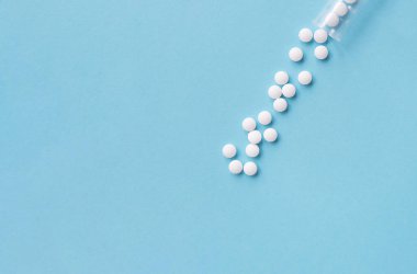 Farklı beyaz haplar ve mavi arka planda plastik bir kap. Tıbbi tema.