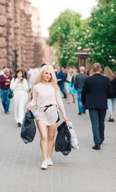 Şehrin arka sokaklarında sokak kıyafetleri içinde mutlu bir kadın. Alışveriş torbaları..