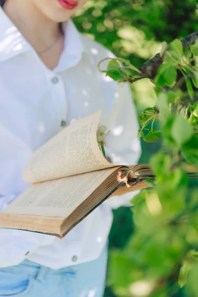 Girl White Blouse Blue Jeans Stands Flowering Tree Reads Book — ストック写真