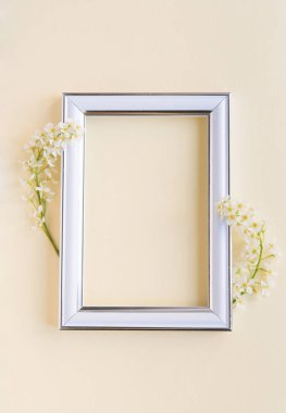 Beyaz kuş kirazının iki dalı boş beyaz bir fotoğraf çerçevesinin yanında sade, hassas bir pastel arka planda..